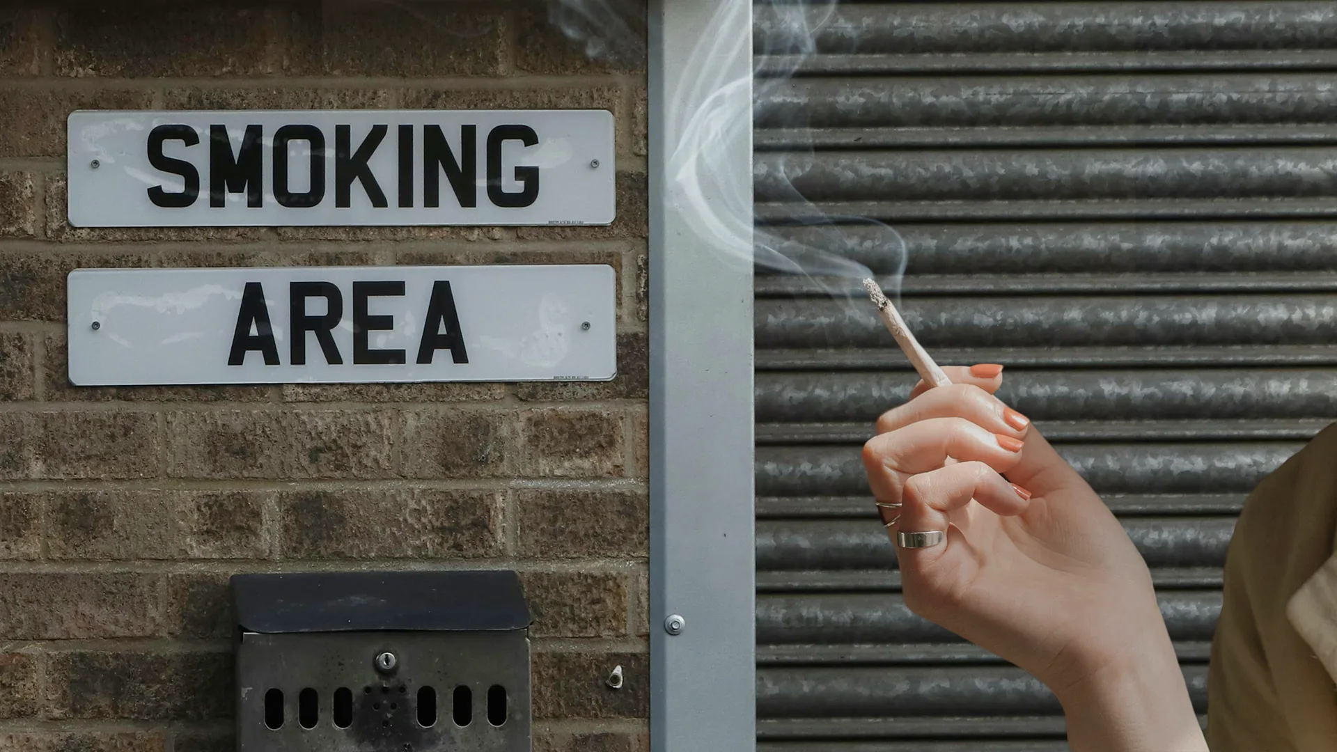 Woman's hand holding a joint near a sign that reads 'smoking area'.