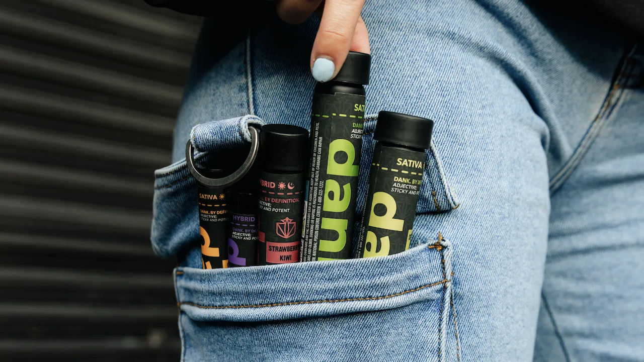 Close up of woman's jeans pockets full of Dank By Definitions pre-rolls containers.