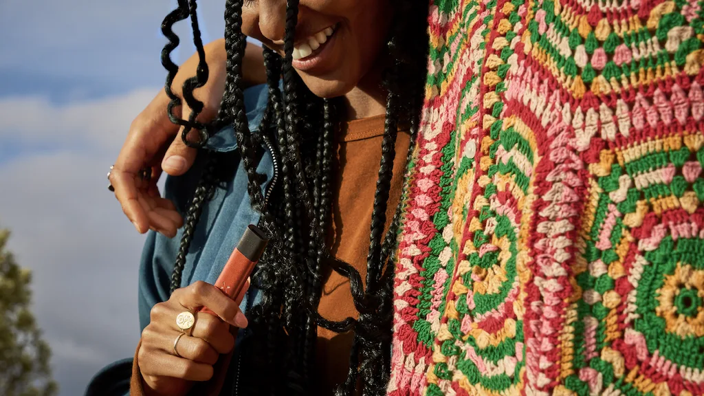 Hippy woman with dreads holding a red disposable vape pen.