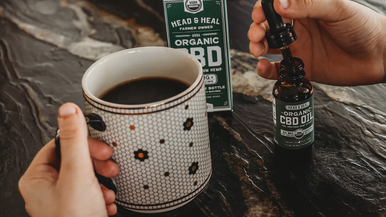 Holding a cup of black coffee next to a Head & Heal tincture dropper bottle.