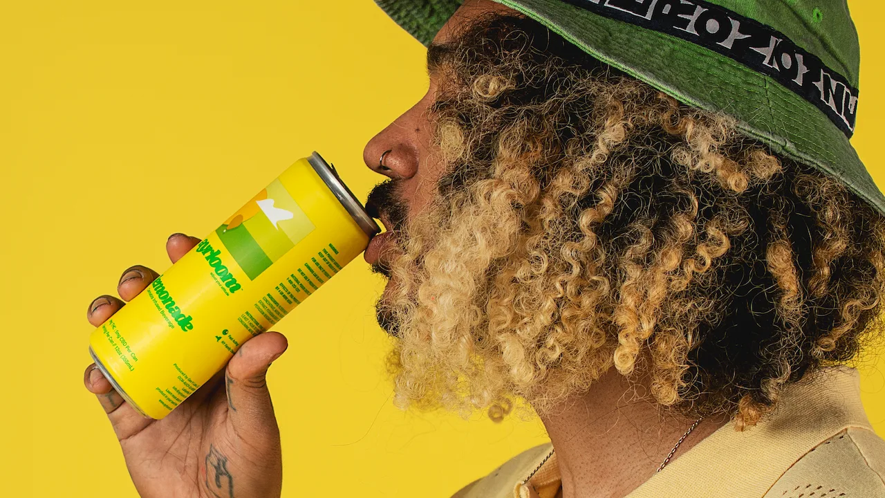 Man with curly hair and a bucket hat sipping a cannabis infused drink.