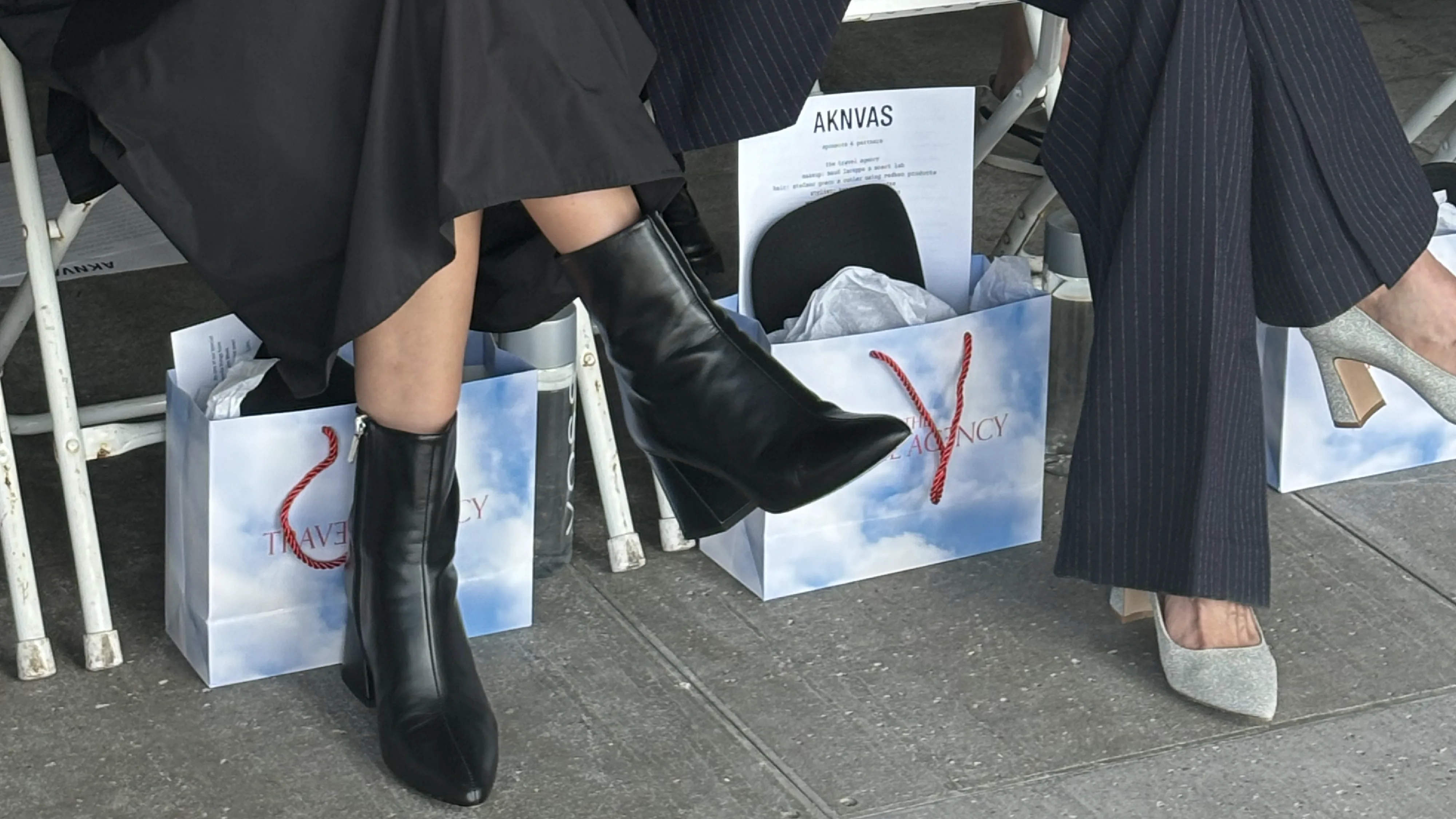 Fashion show attendees with stylish boots and heels at The Travel Agency event during New York Fashion Week, with branded shopping bags.